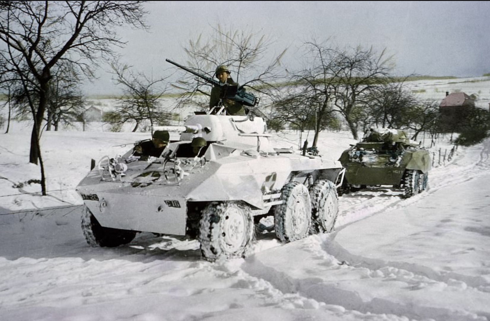 Two tanks, both Light Armored Car M8, roll across a field. 